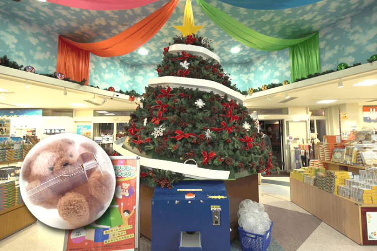 クリスマスツリーの形をした巨大ガチャ。左下にクマのぬいぐるみ入りカプセル